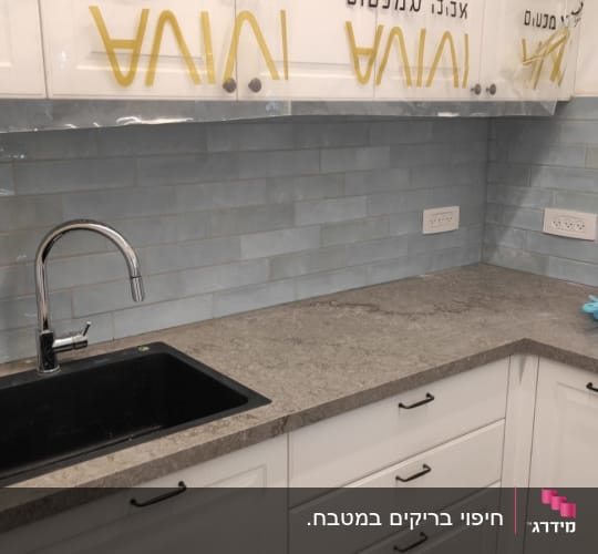 חיפוי קיר מטבח באריחי קרמיקה בגוון תכלת מעל משטח עבודה